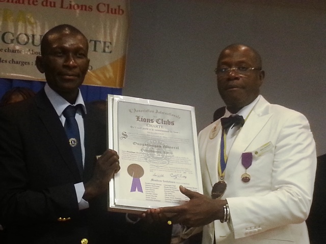 Fabrice Yago en noir recevant la charte des mains du gouverneur