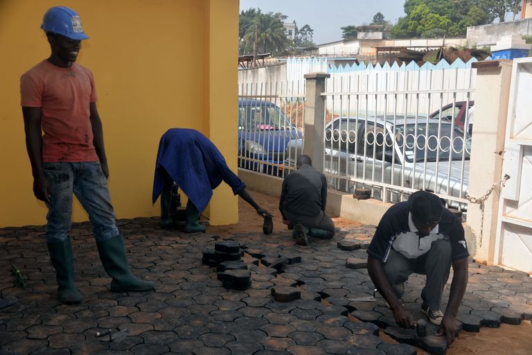 Des jeunes Camerounais procédant à la pose des pavés confectionnés à base de déchets plastiques et de sable. © lemonde.fr